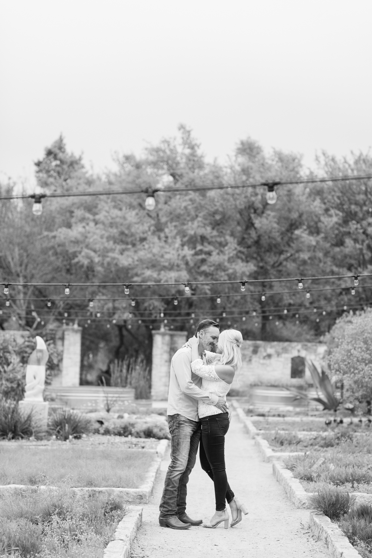The couple stops under the string lights to embrace each other.