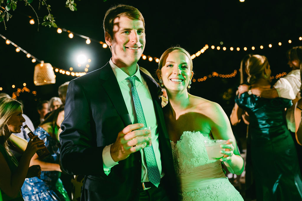 couple smiles while holding drinks at wedding reception