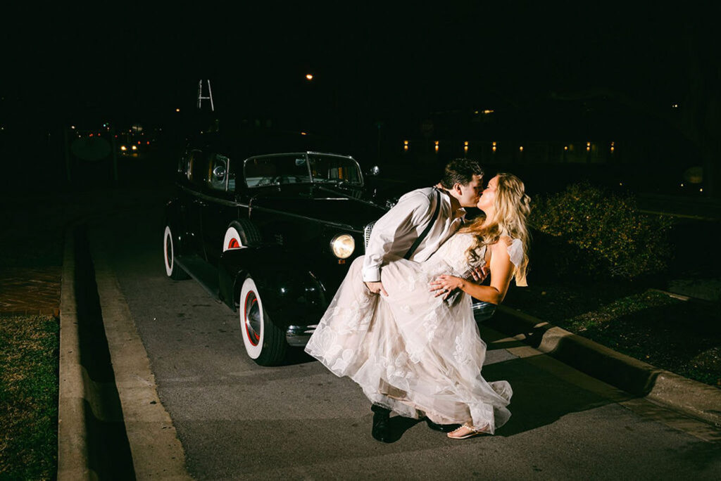 Bride and Groom kiss in front of classic getaway car in front of Woodbine Mansion in Austin